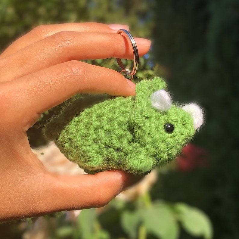May include: Green crocheted triceratops dinosaur keychain with a silver key ring.