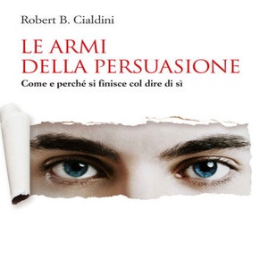 Op de afbeelding: Boekomslag met een witte achtergrond en rode tekst. De titel is "LE ARMI DELLA PERSUASIONE" met de ondertitel "Come e perché si finisce col dire di sì". De auteur is Robert B. Cialdini. De omslag toont een close-up van de ogen van een persoon die rechtstreeks naar de kijker kijkt.