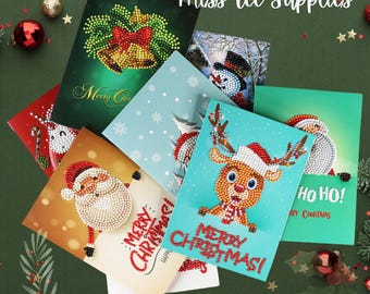 May include: A set of six Christmas-themed diamond painting cards featuring various holiday designs, including a reindeer, Santa Claus, a snowman, and a bell. The cards are all white with colorful diamond-shaped embellishments.
