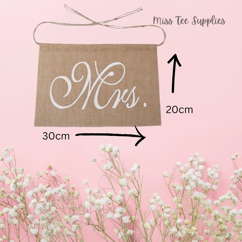 Op de afbeelding: Een jute banner met het woord "Mrs." geschreven in witte, cursieve letters. De banner is 20 cm hoog en 30 cm breed.