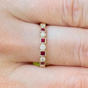 May include: A gold band ring with alternating round and square-shaped gemstones. The round gemstones are white and the square gemstones are red.