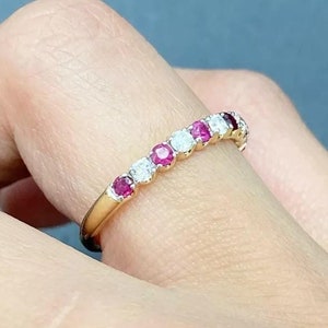 Peut inclure: Une bague en or avec des rubis rouges et des diamants blancs alternés. La bague est sur un doigt.