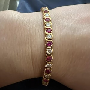 May include: A gold bracelet with alternating red rubies and white diamonds. The bracelet is on a person's wrist.