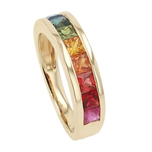 May include: A gold ring featuring a row of square-cut gemstones in a rainbow of colors. The gemstones include blue, green, yellow, orange, red, and pink. The ring has a smooth, polished finish and a classic design.