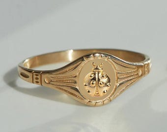 Può includere: Anello dorato con un design dettagliato a coccinella. L'anello ha un centro ovale con la coccinella e una fascia con elementi decorativi. L'anello è probabilmente in oro o in metallo dorato.