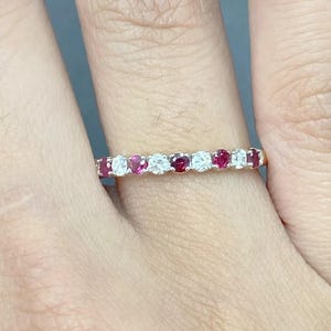 以下が含まれることがあります： 磨かれた金属のバンドに、交互に赤いルビーと白いダイヤモンドがセットされた、繊細なエタニティバンドリングです。