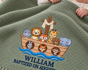 May include: A sage green knitted baby blanket featuring an embroidered Noah's ark with various cartoon animals, including a lion, giraffe, and elephant. The text reads WILLIAM BAPTIZED ON AUGUST, 2026 in dark blue thread on the lower section.
