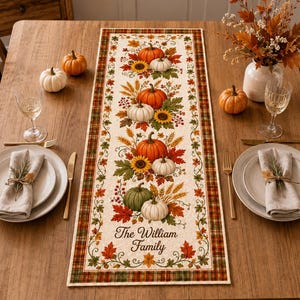 May include: A rectangular table runner featuring a cream-coloured centre with a repeating vertical pattern of orange, white, and green pumpkins, sunflowers, wheat stalks, and autumn leaves. The text The William Family is printed in brown script.