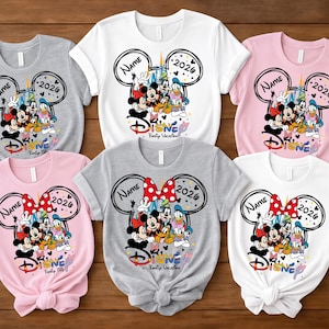 Puede incluir: Camisetas de varios colores con un diseño de vacaciones familiares de Disney. Cada camiseta muestra un contorno de la cabeza de Mickey Mouse con los textos "Name" y "2026". Las camisetas muestran personajes de Disney y la palabra "Disney".