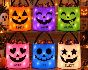 May include: Six cylindrical Halloween candy buckets with black handles and LED lights. Each bucket features a unique black face design and a personalized name: Harper, Mason, Jackson, Avery, Lily, or Elliott. The buckets are filled with candy.
