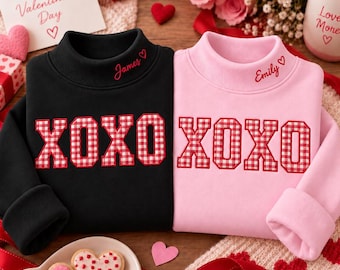 May include: A black sweatshirt and a light pink sweatshirt, each featuring a mock neck and the embroidered red text "James" or "Emily" with a heart. Both garments display the large red and white gingham applique text "XOXO".