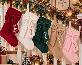 May include: Five velvet Christmas stockings hanging in a row, each featuring a large decorative bow and a personalized name embroidered on the cuff. The colors are deep red, cream, dark green, tan, and light pink, with names Daddy, Mommy, Emma, William, and Sophia.