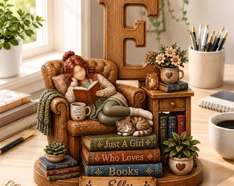 May include: A decorative figurine featuring a person reading in a brown armchair, set against a large wooden letter E. The base includes stacked books labeled Just A Girl Who Loves Books and Elly, a sleeping cat, a mug, and potted plants.