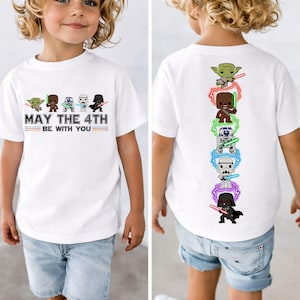 以下が含まれることがあります： スターウォーズのキャラクターと「MAY THE 4TH BE WITH YOU」の文字が入った白いTシャツ。Tシャツの前面にはヨーダ、ウーキー、ストームトルーパー、ダース・ベイダーが描かれています。背面には同じキャラクターが描かれています。