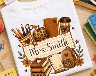 May include: A white t-shirt featuring a graphic illustration of school supplies including a notebook, a backpack, a coffee cup, pencils, scissors, and an apple, all decorated with brown leopard print and gingham patterns, with the text Mrs. Smith.