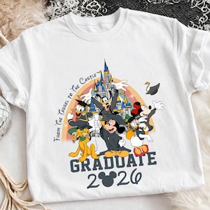 Könnte beinhalten: Weißes T-Shirt mit einer farbenfrohen Grafik von Disney-Figuren in Abschlusskleidung. Das Design umfasst einen Regenbogen, ein Schloss und den Text "From the Tassel to the Castle" und "Graduate 2026".