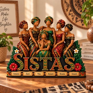 Puede incluir: Una figura decorativa que muestra a seis mujeres con vestidos y pañuelos estampados, situadas detrás de una base con la palabra SISTAS en letras grandes. La base incluye seis pequeñas placas etiquetadas Amara, Zuri, Nia, Amani, Kiana e Imani.