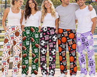 May include: Five pairs of custom pajama pants featuring sports themes. The first pair is white with baseballs, gloves, and the name Sophia 35. The second is green with footballs and the name Emma 99. The third is black with soccer balls and the name Olivia 28. The fourth is black with basketballs and the name Mason 12. The fifth is purple with volleyballs and the name Logan 23.
