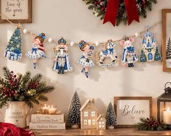 May include: A Christmas garland featuring hanging cutouts of a decorated tree, a ballerina, a nutcracker, a girl holding a nutcracker, a rocking horse, a mouse, and a castle, all in blue and white, strung on a white pom-pom rope.