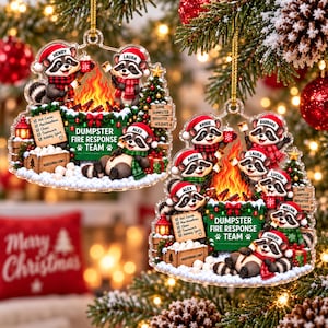 May include: Two clear acrylic Christmas ornaments featuring cartoon raccoons wearing Santa hats and scarves around a campfire. The green dumpster is labeled DUMPSTER FIRE RESPONSE TEAM with a list of items and a crate of marshmallows.