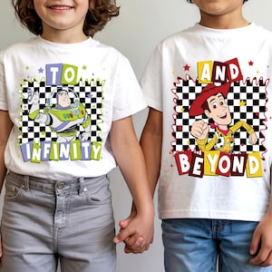 May include: Two white t-shirts with cartoon graphics. One shirt features Buzz Lightyear with the text "TO INFINITY" and the other shirt features Woody with the text "AND BEYOND". Both shirts have a black and white checkered background.