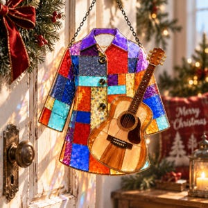 Könnte beinhalten: Ein hängendes Buntglas-Ornament in Form eines Hemdes mit Kragen, bestehend aus einem Patchwork aus leuchtend roten, blauen, violetten, orangen und gelben Glasstücken, mit drei dunklen Knöpfen und einer kleinen Akustikgitarre auf der Vorderseite.