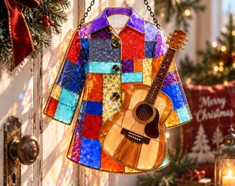 May include: A stained glass hanging ornament shaped like a collared shirt with a patchwork of vibrant red, blue, purple, orange, and yellow glass pieces, featuring three dark buttons and a small acoustic guitar attached to the front surface.
