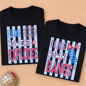 May include: Two black t-shirts with matching designs. One says "I LIKE HOW SHE EXPLODES" with a firework graphic. The other says "I LIKE HOW HE BANGS" with a firecracker graphic. Both have blue and red accents.