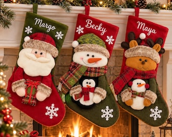 May include: Three Christmas stockings featuring embroidered names Margo, Becky, and Maya. The first is green with a Santa Claus, the second is red with a snowman and penguin, and the third is red with a reindeer and snowman, all with white snowflakes.