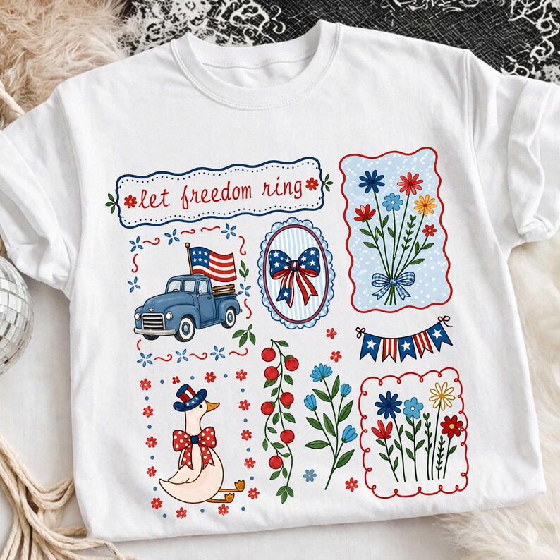May include: White t-shirt with patriotic illustrations. Features a blue truck with an American flag, floral bouquets, a goose in a patriotic hat, and the text "let freedom ring". The design is in red, white, and blue.