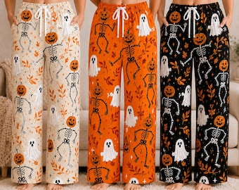 May include: Three pairs of wide-leg lounge pants featuring a Halloween pattern of skeletons with pumpkin heads, white ghosts, and orange leaves. The pants are available in cream, orange, and black, each with a white drawstring waist tie.