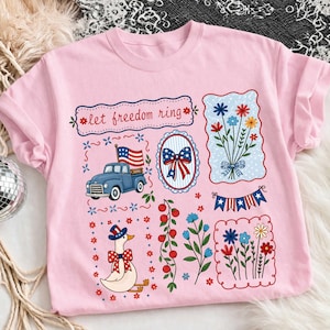 May include: Pale pink t-shirt with patriotic designs. Includes a blue truck with an American flag, a floral bouquet, and a goose in a hat and bow tie. The words "let freedom ring" are printed at the top.