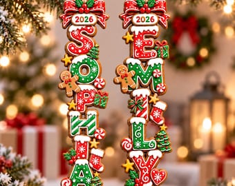 May include: Two vertical gingerbread-style Christmas ornaments featuring the names SOPHIA and EMILY. Each ornament is topped with a red bow, the year 2026, and decorated with icing, small gingerbread figures, stockings, and green trees.