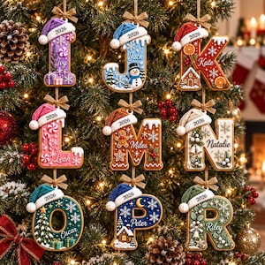 May include: Nine hanging Christmas ornaments shaped as letters I, J, K, L, M, N, O, P, and R. Each letter features a unique holiday theme, a knit hat with the year 2026, and a personalized name. The ornaments are suspended by small brown bows.