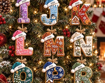 May include: Nine hanging Christmas ornaments shaped as letters I, J, K, L, M, N, O, P, and R. Each letter features a unique holiday theme, a knit hat with the year 2026, and a personalized name. The ornaments are suspended by small brown bows.