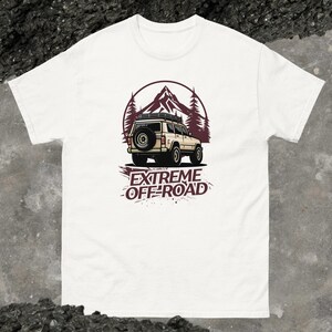 May include: White t-shirt featuring a graphic of a beige off-road vehicle driving through a mountain landscape. The text "EXTREME OFF-ROAD" is printed below the vehicle.