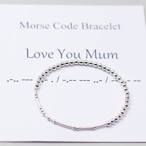Può includere: Braccialetto con perline d'argento con il messaggio "Love You Mum" in codice Morse. Il braccialetto è su una carta bianca con le parole "Morse Code Bracelet" stampate su di essa.