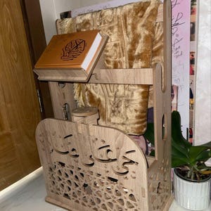 Moroccan Islamic prayer corner organizer in use — Quran on built-in stand, prayer clothes and tasbih holder. Complete Islamic home decor piece with arabesque carvings and Arabic calligraphy. Handcrafted in Morocco.