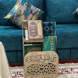Moroccan Islamic prayer corner organizer in traditional Moroccan living room with zellige tiles. Quran stand, Islamic books storage and prayer mat holder. Carved wood MDF with arabesque cutouts and Arabic calligraphy. Authentic Islamic home decor handcrafted in Morocco.