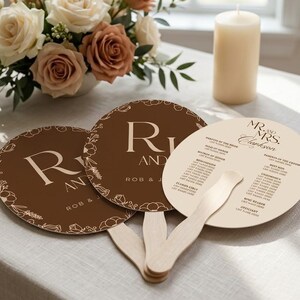 May include: Three round wedding program fans with wooden handles. Two fans are dark brown with white floral outlines and the text R and J Rob & J. One fan is cream-colored with black text listing the wedding party and Mr. and Mrs. Clarkson.
