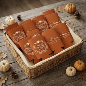 May include: A collection of burnt orange foam can coolers arranged in a woven basket. Some coolers feature a circular wreath design with the text Thankful Grateful Blessed, while others are personalized with Johnson Family Thanksgiving 11.26.2026.