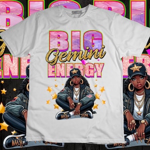 May include: White t-shirt with the text "BIG Gemini ENERGY" in gold and pink lettering. The graphic features a cartoon illustration of a woman wearing a star cap, gold jewelry, and a black jacket. Gold stars are scattered around the illustration.