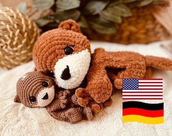 May include: Two crocheted stuffed toys, a brown bear and a smaller brown otter, are cuddling together on a white fluffy surface. The bear has a white snout and black eyes. The otter has black eyes and a brown snout. The background is blurred and out of focus.