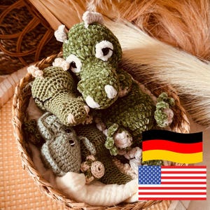 May include: A selection of handmade crochet dinosaur toys in a woven basket. The dinosaurs are various shades of green with white and beige accents. The basket is lined with white fabric and set against a neutral background.