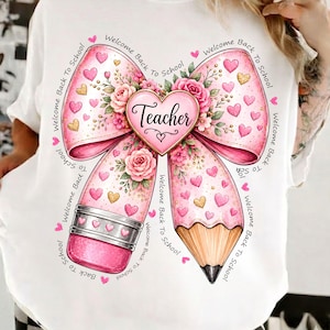 May include: A white t-shirt featuring a graphic of a large pink bow shaped like a pencil, decorated with pink roses, small hearts, and the word Teacher inside a heart. The text Welcome Back To School is printed in a circular pattern around the design.