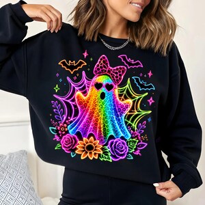 May include: A black long-sleeved sweatshirt featuring a vibrant, multi-coloured ghost graphic with a leopard print pattern, heart-shaped sunglasses, and a polka-dot bow. The design includes neon-coloured spiderwebs, bats, flowers, and stars.