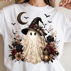 May include: A white t-shirt featuring a graphic of a ghost wearing a black lace witch hat, surrounded by dark red and black flowers, a golden crescent moon, flying bats, and a small glowing lantern, creating a detailed seasonal illustration.
