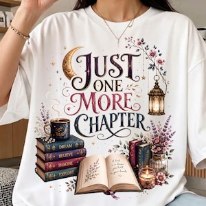May include: A white t-shirt featuring a graphic print with the text "JUST ONE MORE CHAPTER". The design includes a stack of four books labeled "DREAM", "BELIEVE", "IMAGINE", and "EXPLORE", a steaming mug, an open book, a lantern, and flowers.