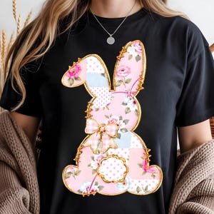May include: Black t-shirt featuring a patchwork bunny design. The bunny is outlined in gold and filled with pink floral patterns, polka dots, and a gingham bow. The design has a vintage, Easter-themed aesthetic.