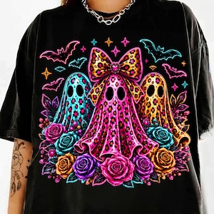May include: A black t-shirt featuring a graphic of three ghosts with leopard print patterns in blue, pink, and yellow. The center ghost wears a large leopard print bow. The design includes colorful roses, small bats, and star shapes surrounding the ghosts.